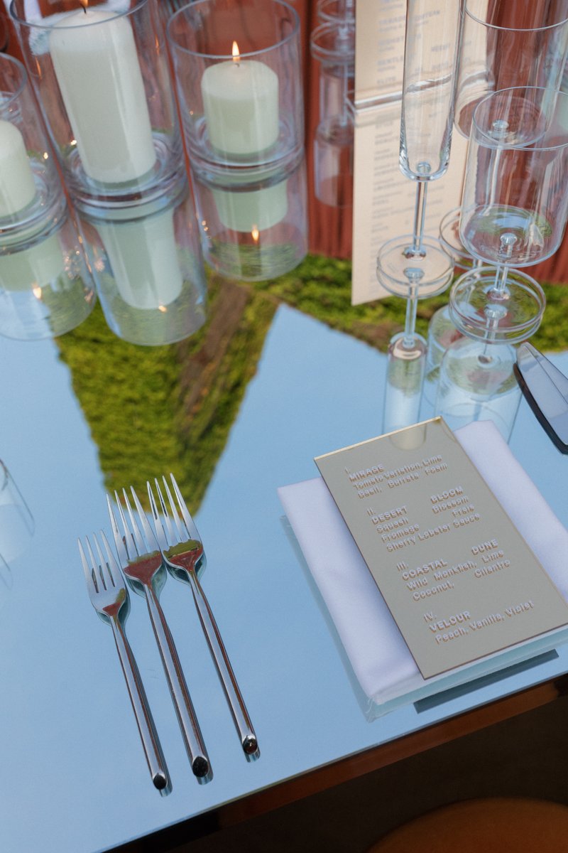 A detailed shot of an elegant table setting features lit candles in glass holders, an array of empty champagne flutes, a