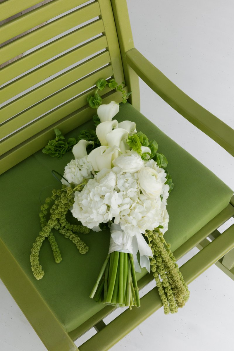 A beautiful white and green floral bouquet rests on a lime green slatted chair. The bouquet features white hydrangeas, c