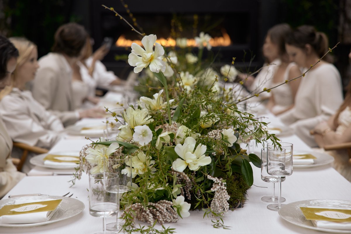 A beautifully arranged long table features a lush floral centerpiece with white and yellow flowers, surrounded by elegan