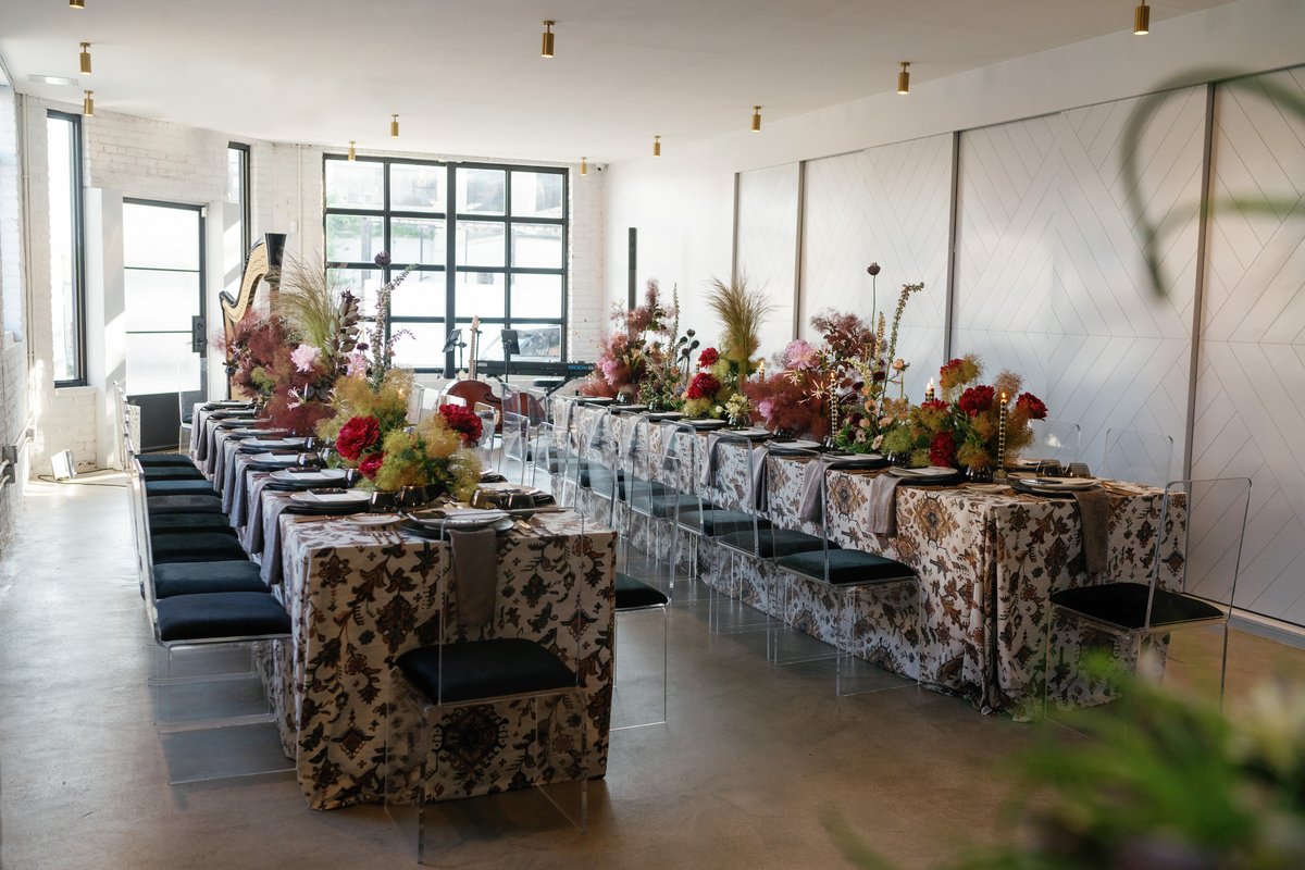 A long, elegantly set dining table stretches across a modern event space, adorned with lush, dramatic floral arrangement