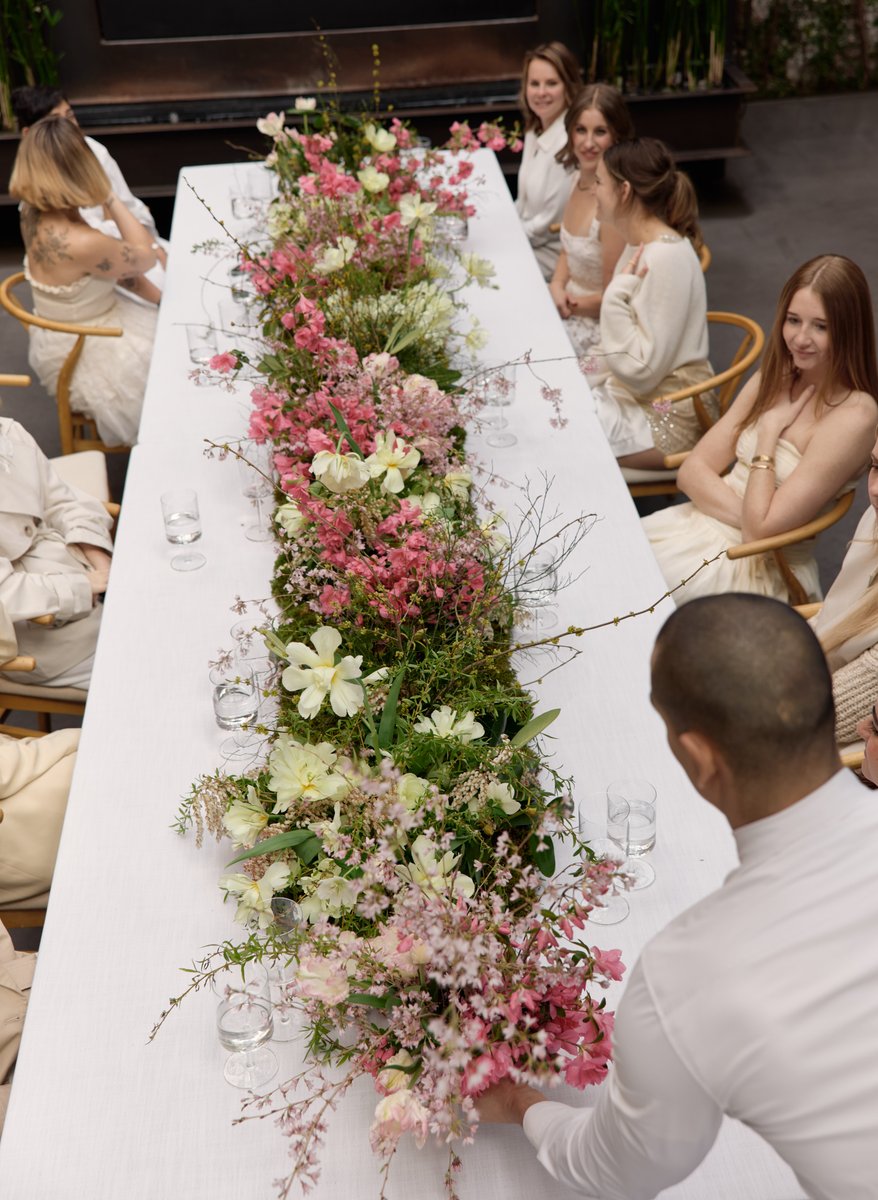 An overhead shot captures a long white dining table adorned with an elaborate, lush floral runner featuring pink and whi