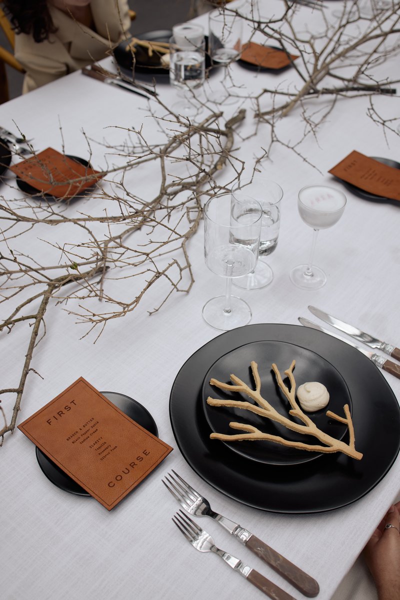 A beautifully styled table setting features minimalist black plates, elegant cutlery, and a unique natural branch center
