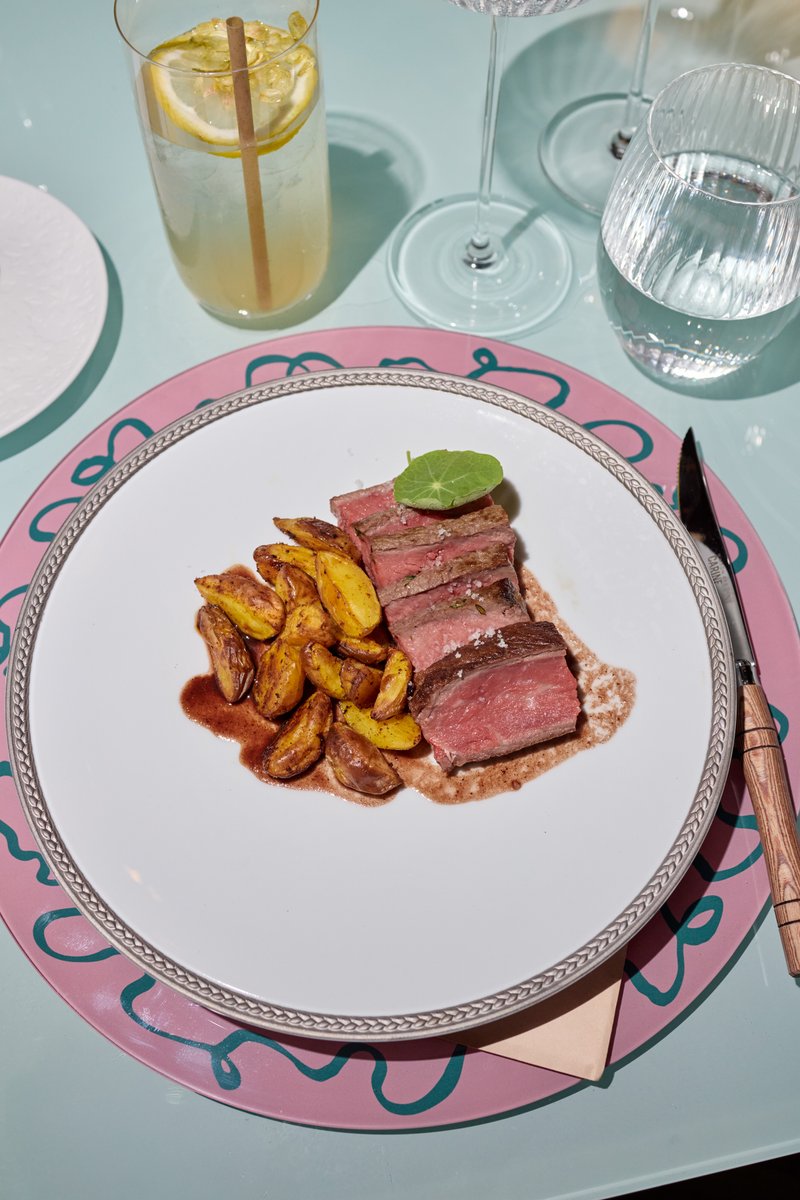 A beautifully plated dish featuring sliced medium-rare steak and roasted baby potatoes with a rich sauce is presented on
