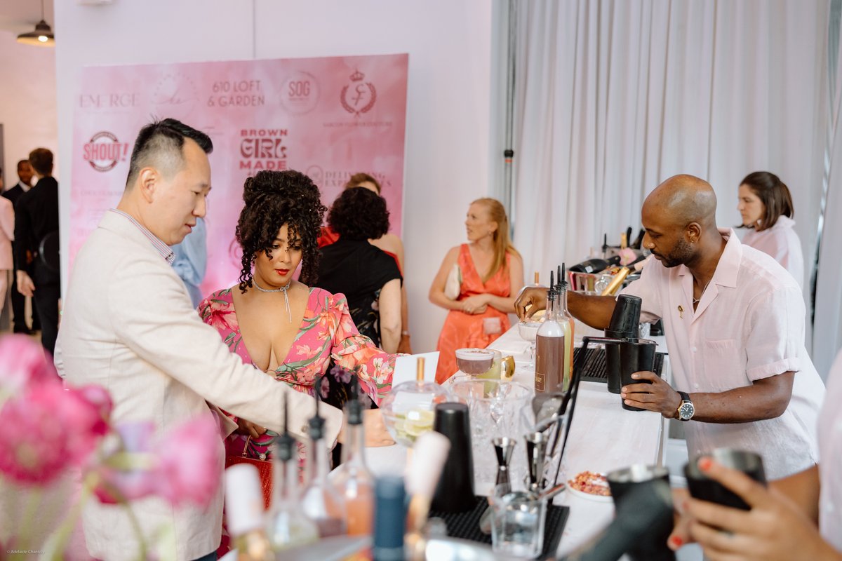 A vibrant cocktail reception is in full swing, with guests gathered around a bustling bar station. A bartender in a ligh