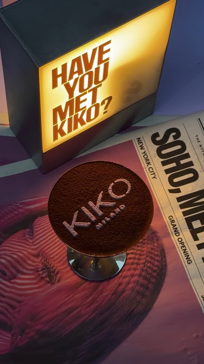A branded cocktail, featuring the 'KIKO Milano' logo dusted on its surface, is presented on a table. Beside it, an illum