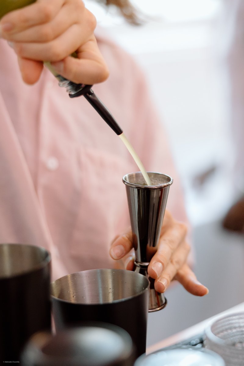 A close-up shot captures a bartender's hands meticulously pouring a light-colored liquid from a bottle with a pourer int