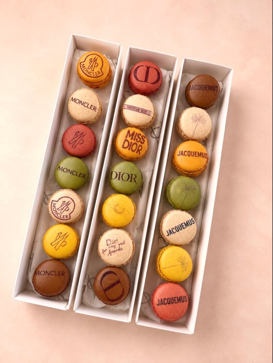 Three rows of colorful macarons, each featuring luxury brand logos like Moncler, Dior, and Jacquemus, are neatly arrange