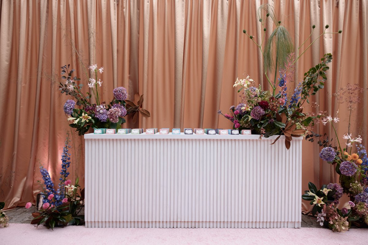 A stylish white fluted bar, adorned with lush, colorful floral arrangements on either side, stands against a warm peach-