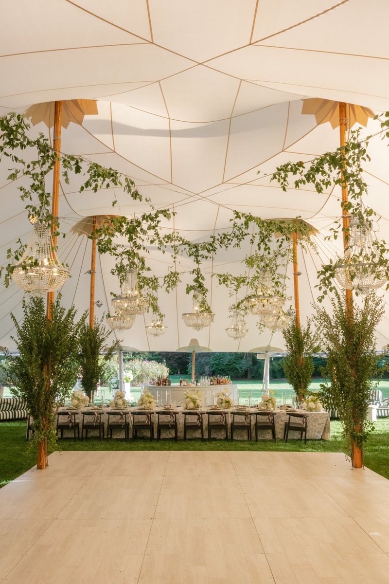 An elegant outdoor event tent is meticulously set up for a reception, featuring a light wood dance floor in the foregrou
