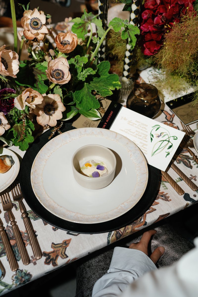 A beautifully arranged close-up of a formal table setting, featuring a delicate first course dish with edible flowers, s