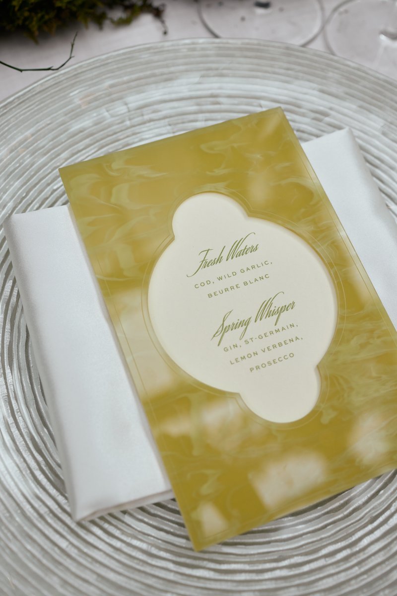 A close-up shot of an elegant place setting featuring a textured clear charger plate, a folded white napkin, and a styli