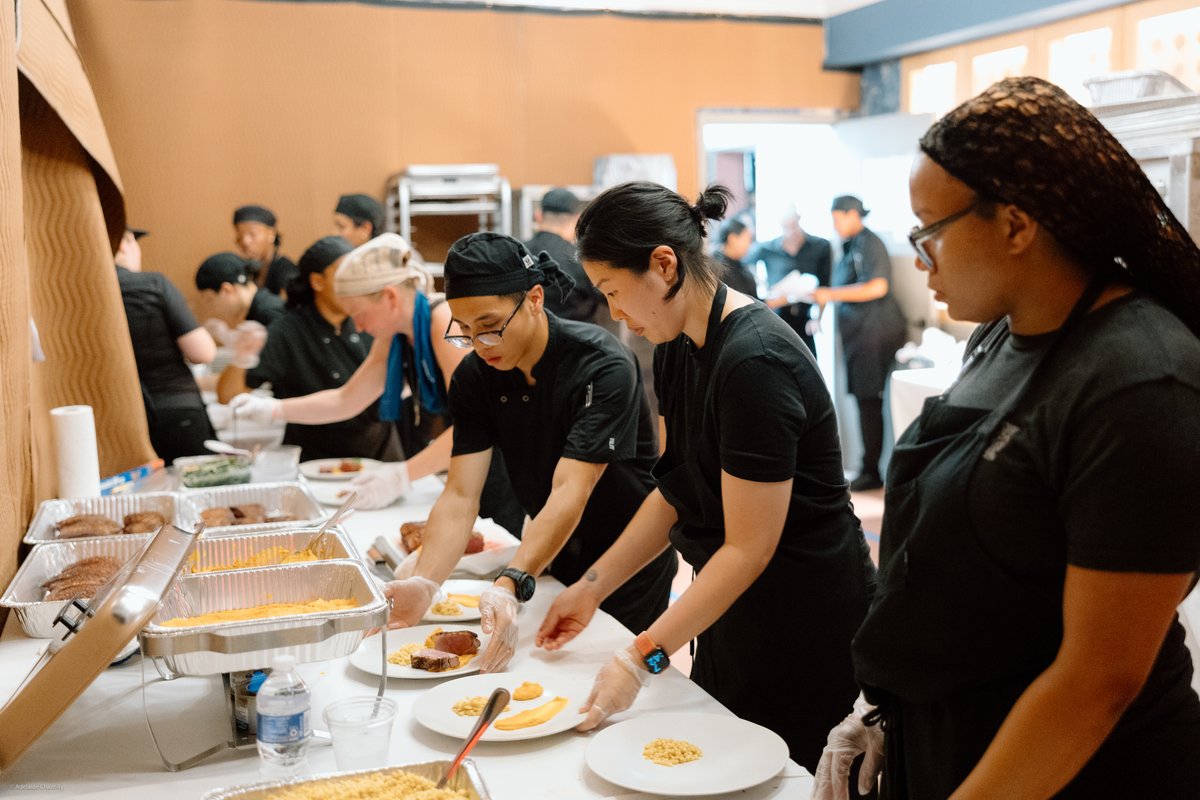A team of catering staff, dressed in black uniforms and wearing gloves, are meticulously plating individual portions of 