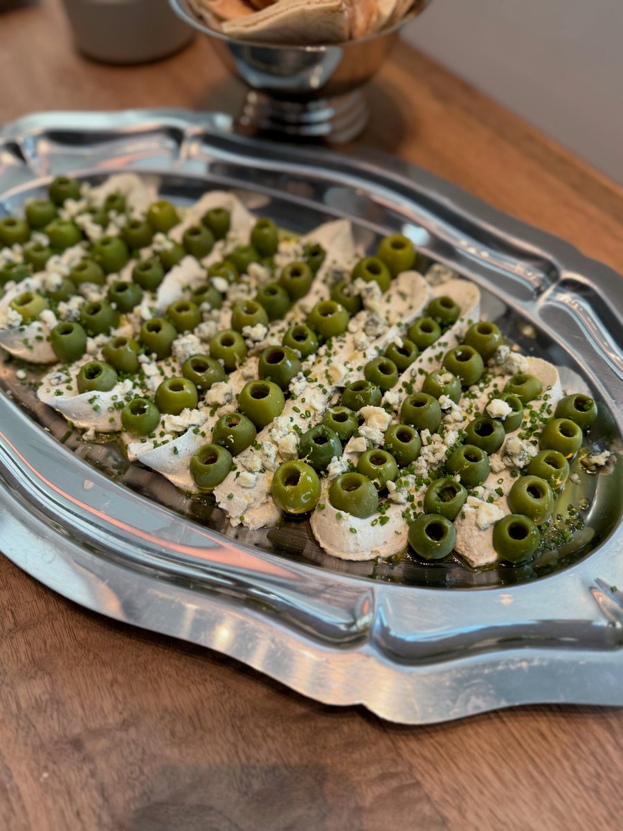 A close-up shot of an elegant appetizer platter featuring individual servings of a creamy spread topped with green olive
