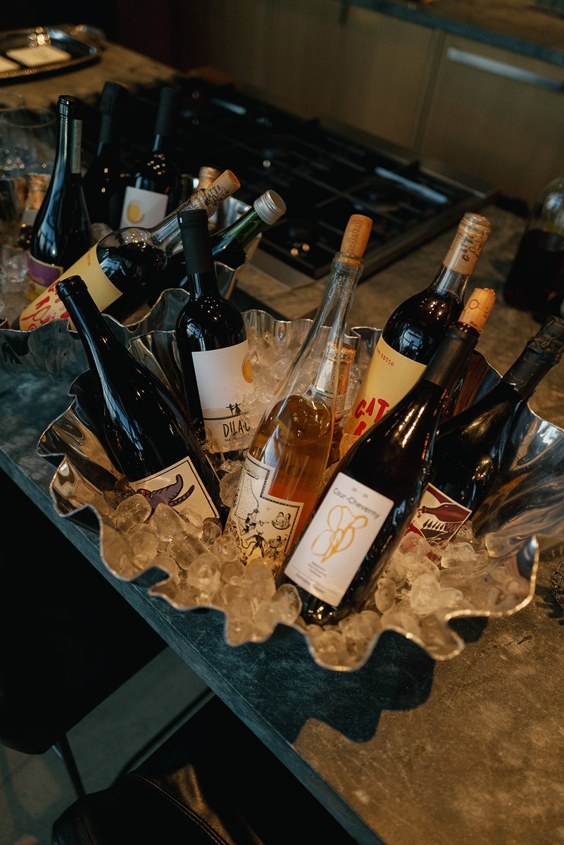 A variety of wine bottles, including red, white, and rosé, are chilling in a large, silver, shell-shaped ice bucket. The