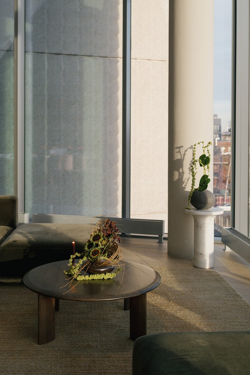 This photo captures a modern lounge area bathed in natural light, featuring a dark wood coffee table with an elaborate f