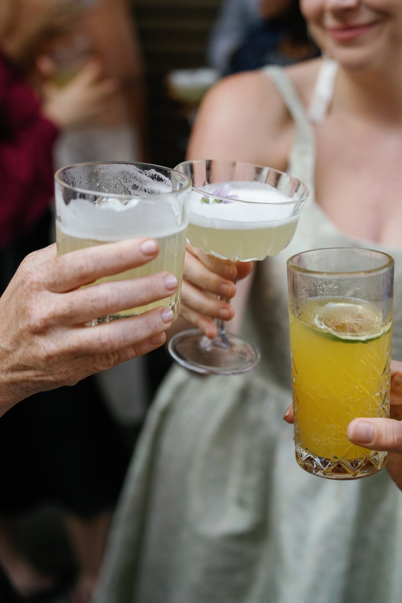 Three different cocktails are held by guests, appearing to be in a toast or social gathering. The close-up shot captures
