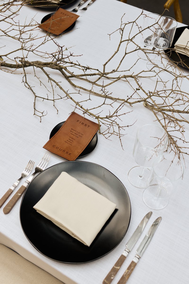 A beautifully arranged table setting features a stark white tablecloth, matte black plates, and elegant cutlery with mar