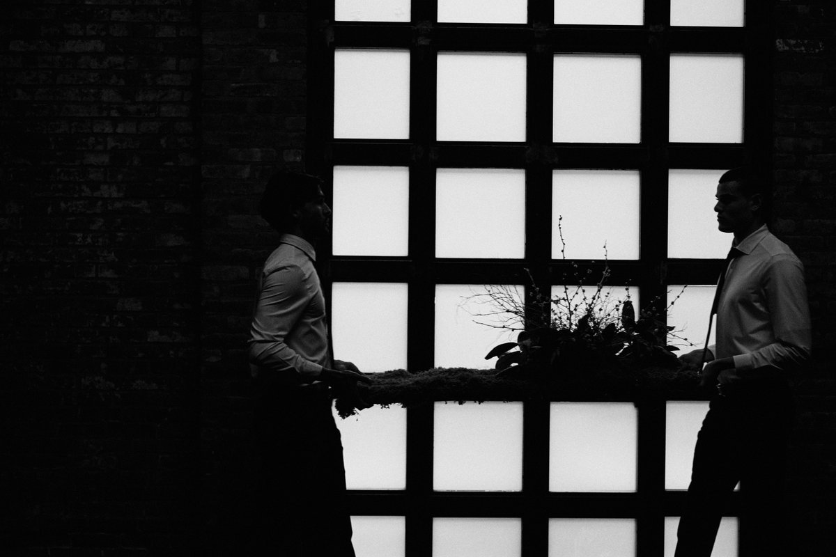 Two event staff members are captured in dramatic silhouette against a large grid-paned window, appearing to be in the pr