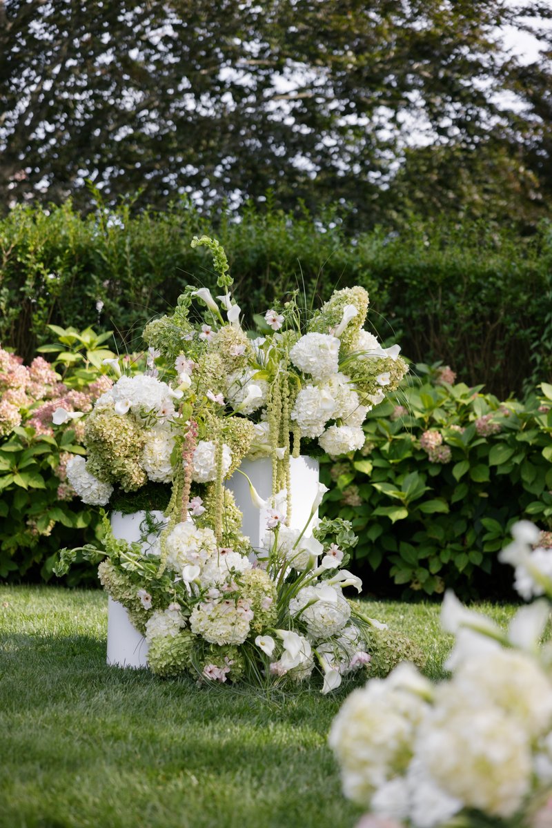 A beautiful and elaborate floral arrangement in shades of white and green is showcased on white pedestals on a vibrant g