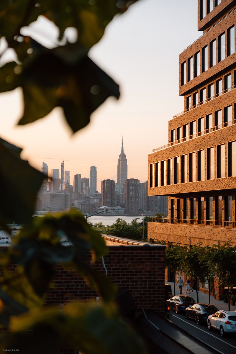 A scenic wide-shot captures the Manhattan skyline, including the Empire State Building, bathed in the warm glow of golde