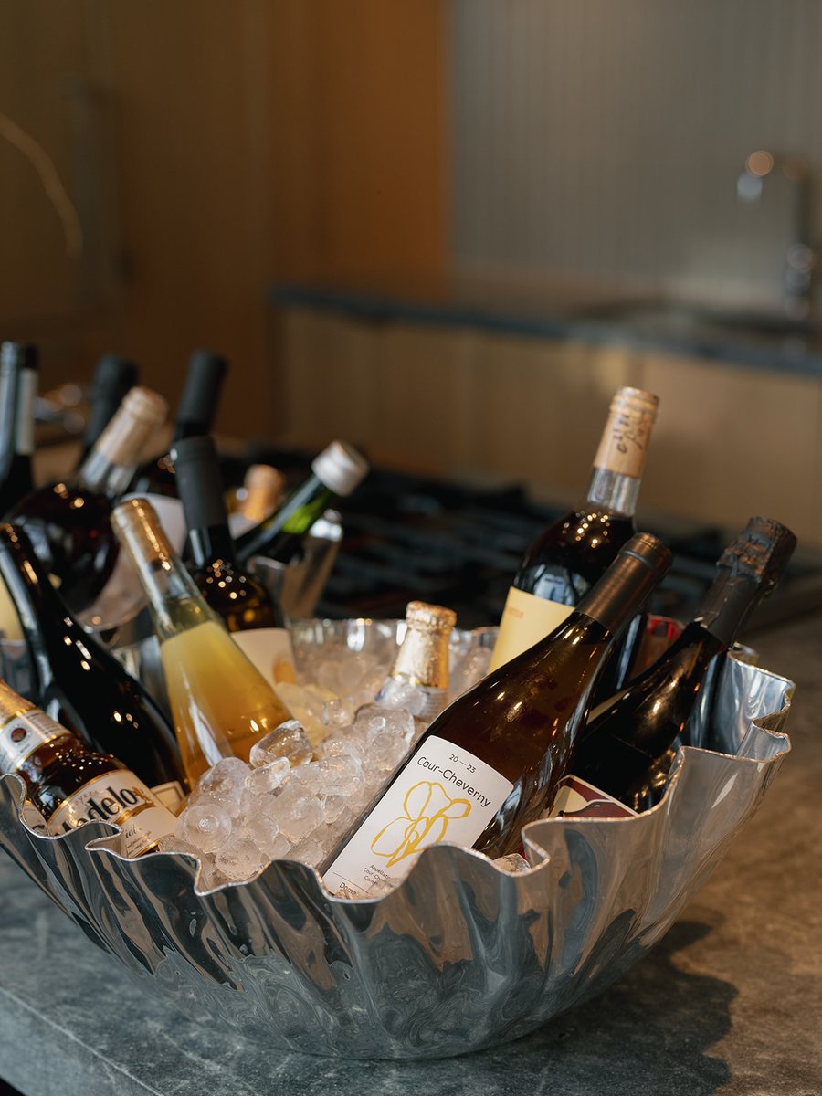 A variety of wine, beer, and other bottled beverages are presented in a stylish, fluted silver ice bucket, filled with i