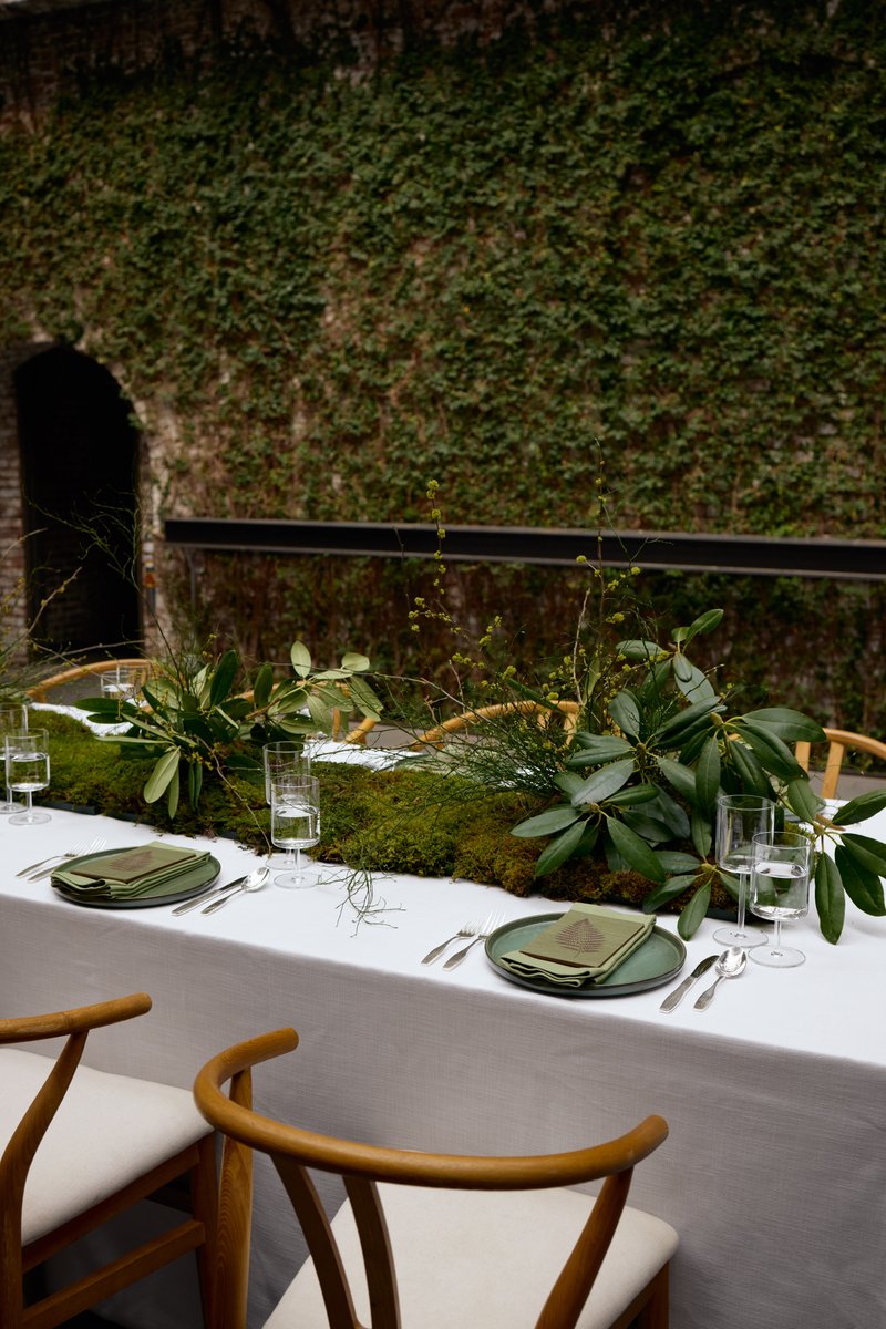 A beautifully set dining table features a lush, natural centerpiece made of moss and various green foliage, creating an 