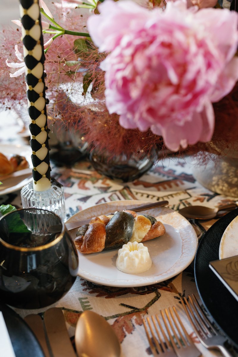 A close-up shot of an elegantly set table, featuring a multi-colored braided bread roll with a molded butter pat on a wh