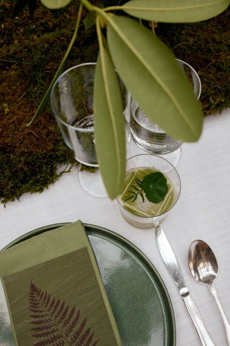 A close-up shot of an elegantly set table, featuring a green-themed place setting with a ceramic plate, a fern-patterned