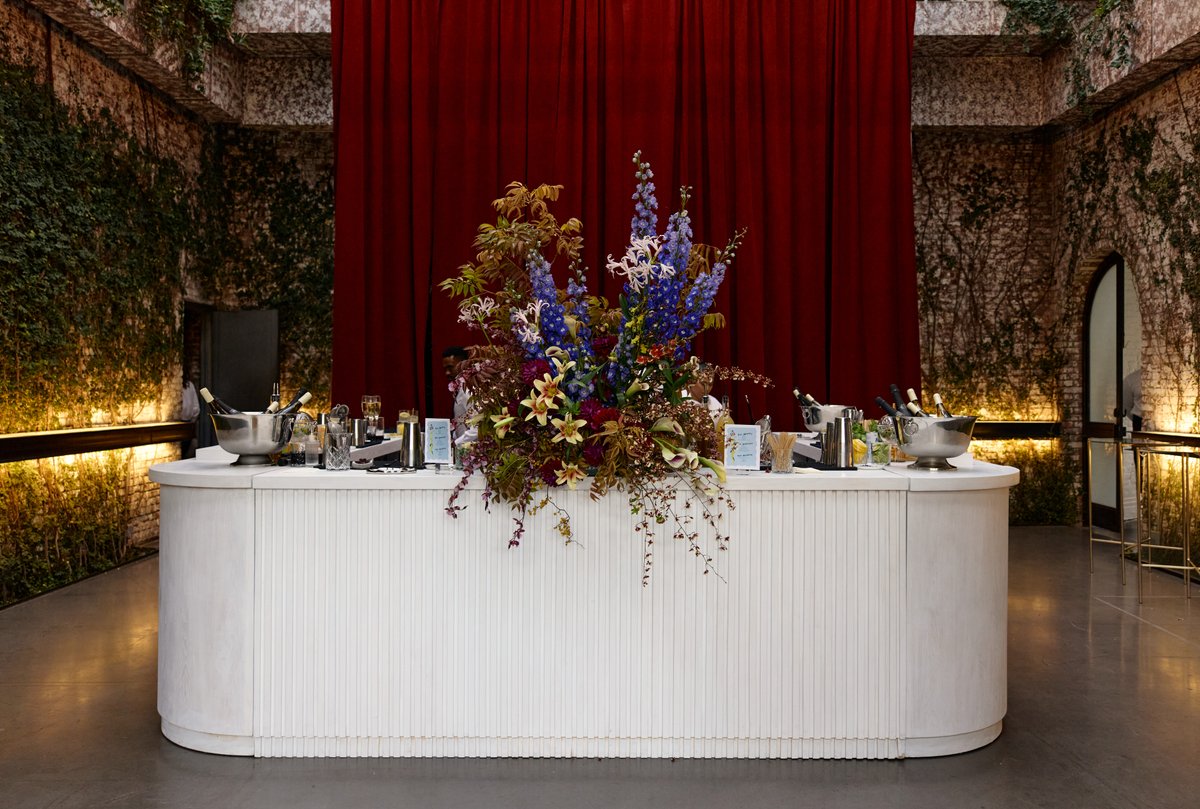A beautifully arranged bar station is set up in a unique venue, featuring a large floral centerpiece. The white fluted b