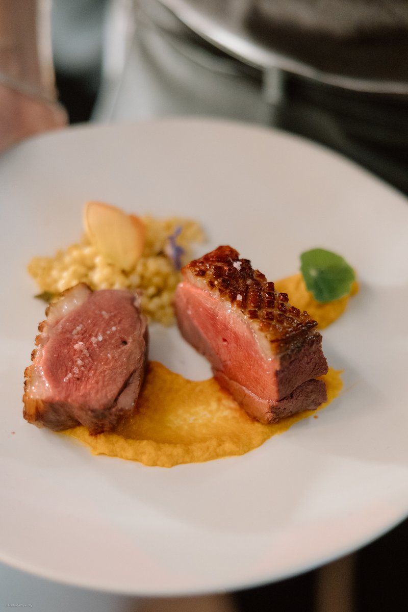 A meticulously plated dish features two slices of perfectly cooked duck breast, garnished with flaky sea salt, alongside