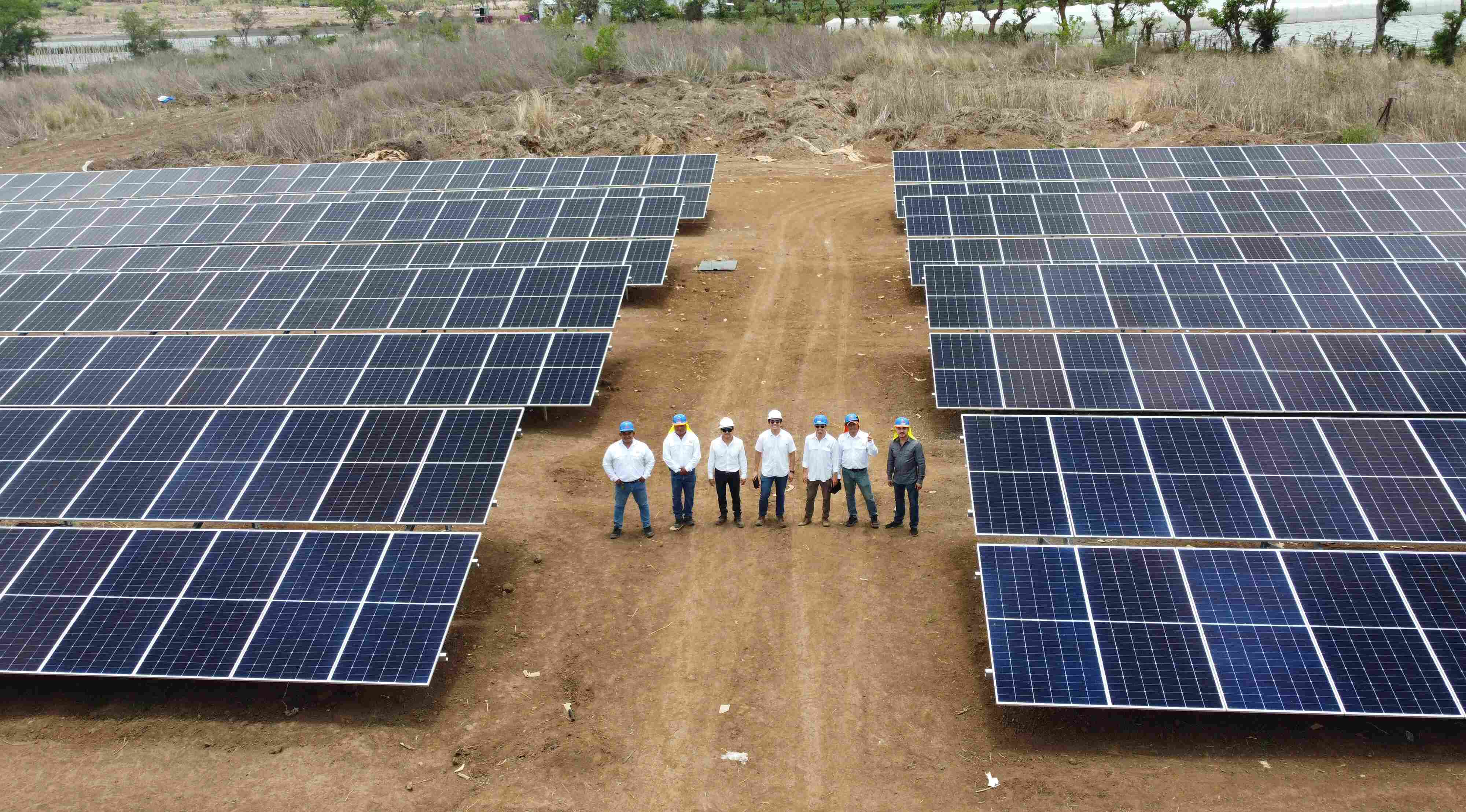 Equipo de obra con cascos formado en el camino entre dos filas de paneles solares en construcción
