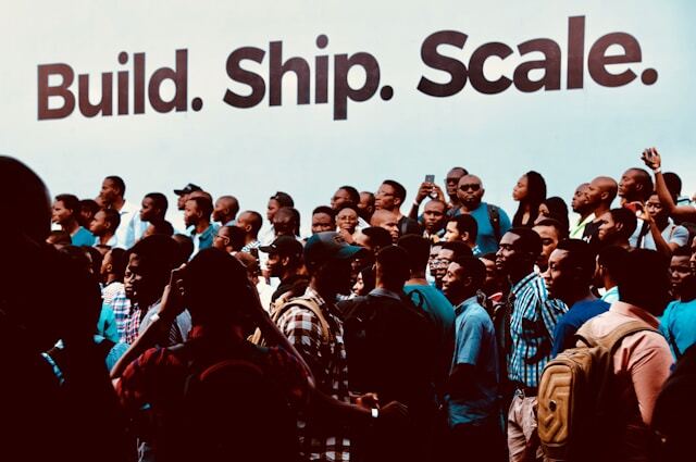 Crowd of people in front of wall with writing "Build, ship, scale." Photo by Desola Lanre-Ologun.