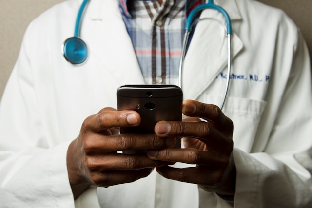 Doctor in lab coat holding a smartphone. Photo by National Cancer Institute.