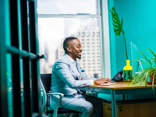 Man wearing suit and smiling while seated in front of a iMac. Photo by Jopwell.