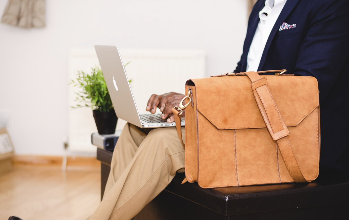 Man sitting with his laptop on his lap with a laptop bag on a stool beside him