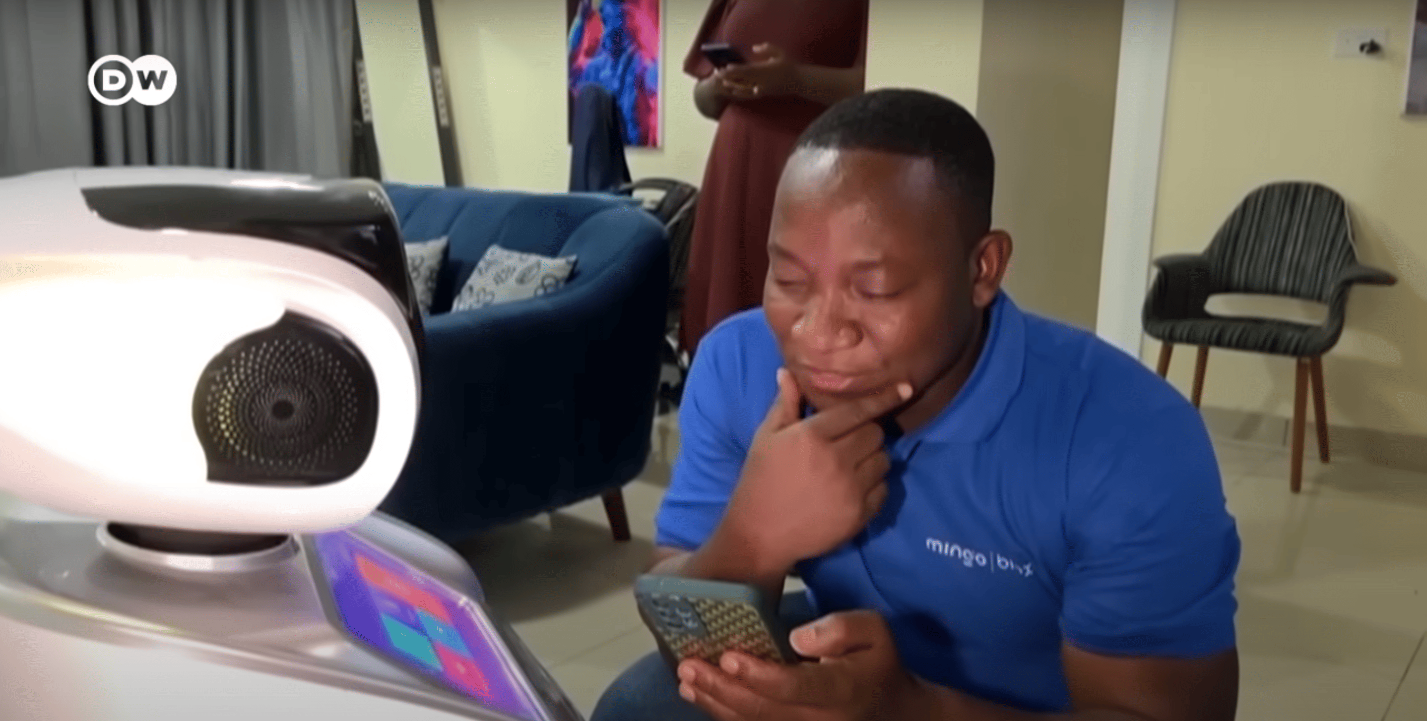 Man squatting in front of a robot, looking at his phone to give the robot instructions.