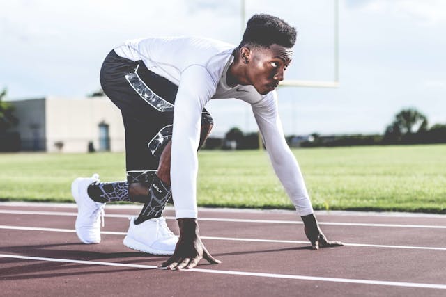 Focused athlete in starting position on a sunny track field, ready to sprint. Photo by nappy on pexels.com.