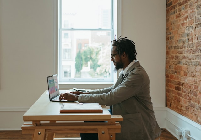 A man in front of the desk and pressing his laptop. Photo by Windows.