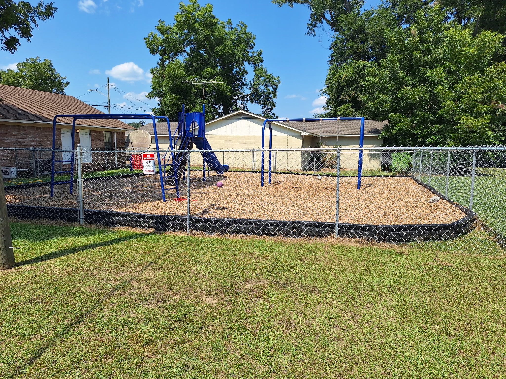 Fenced outdoor playground with swings, climbing equipment, and open play space
