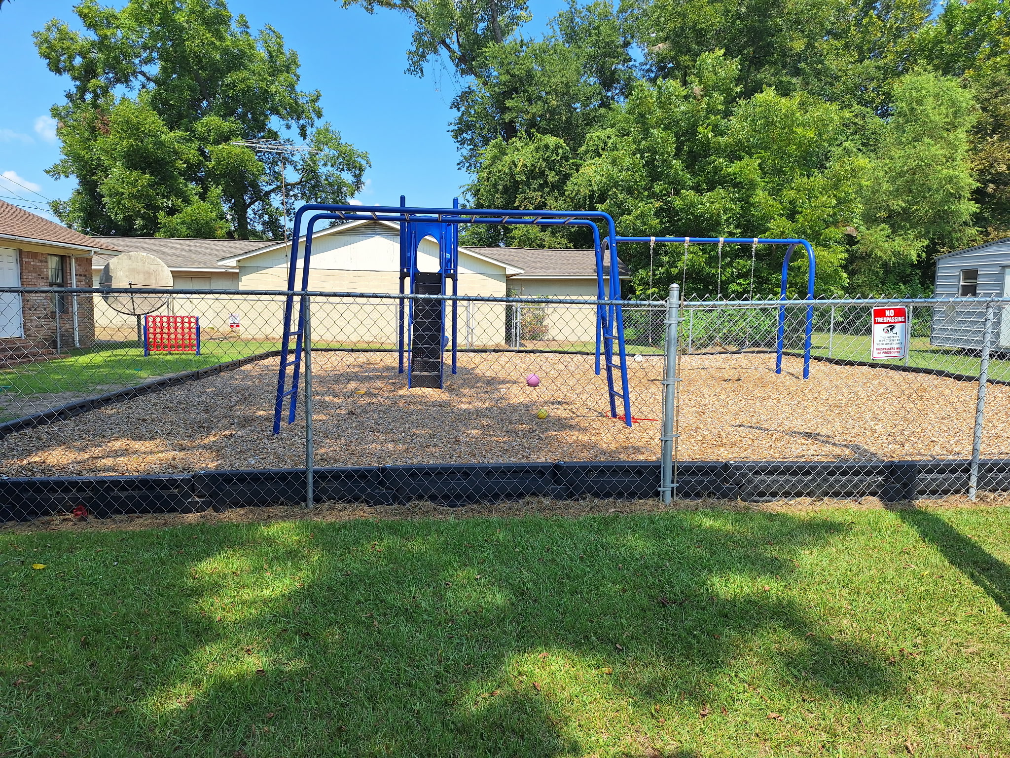 Outdoor playground with blue climbing equipment, swings, and wood-chip play surface