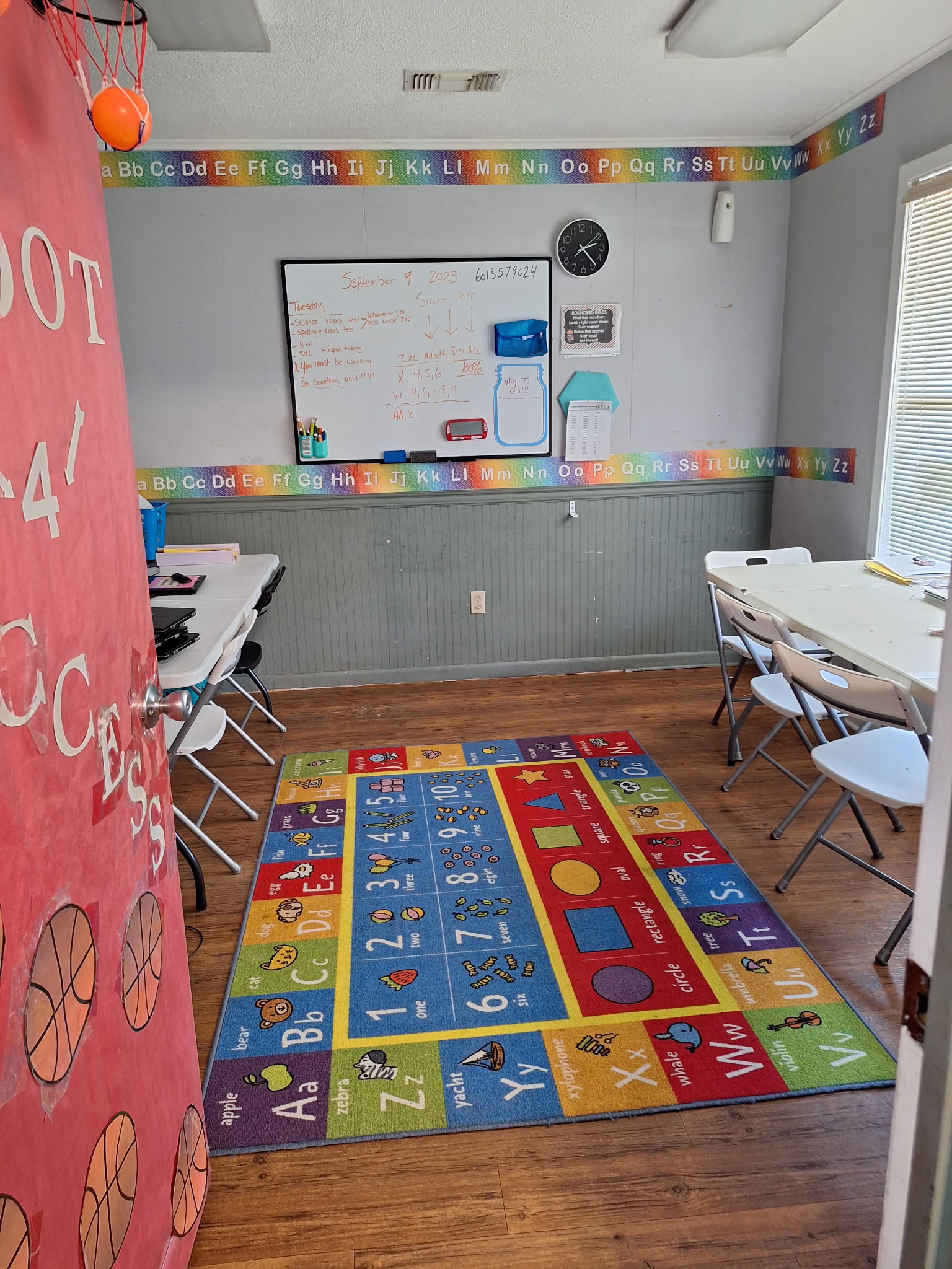 Classroom with child desks, whiteboard, alphabet border, and colorful learning rug