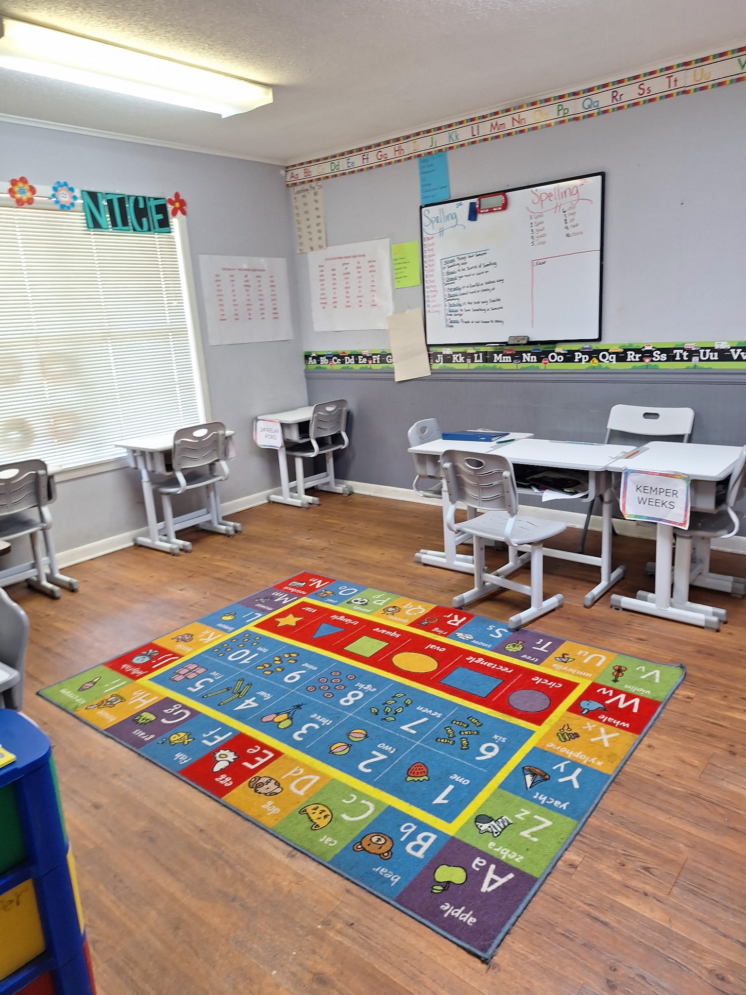 Early learning classroom with desks, whiteboard, spelling notes, and colorful alphabet rug