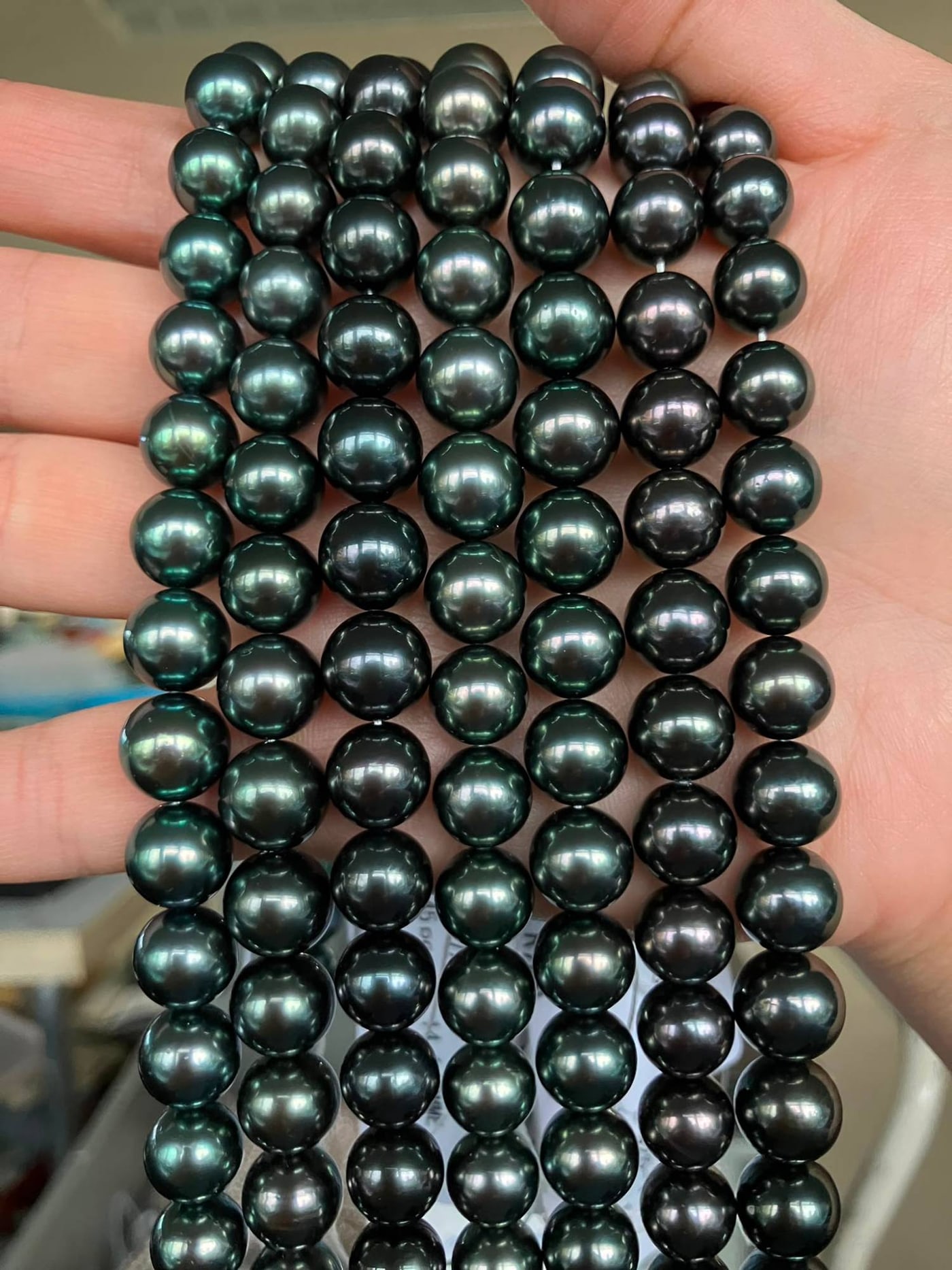 TRUE AAA Tahitian pearl strands held in the hand, showing high luster and green and peacock overtones
