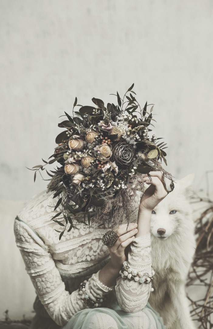 By My Side surreal art print by Donna O’Donoghue featuring a woman hidden behind a floral bouquet seated beside a white wolf.