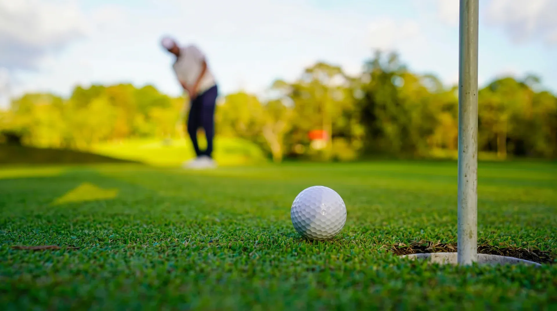 Golf ball near the hole on a green with golfer putting in the background