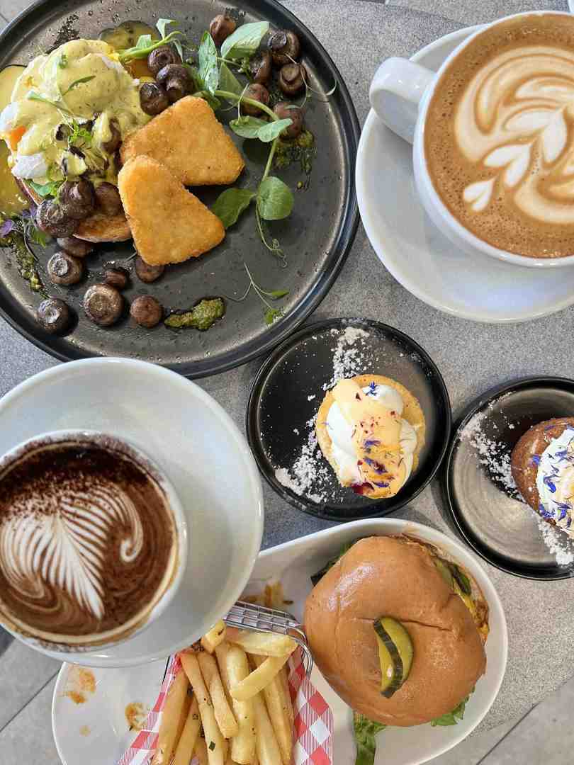 Overhead view of two immaculate coffee cups displaying beautiful feather and tulip latte art, served alongside an amazing brunch spread. Truly the Sunshine Coast's best coffee.