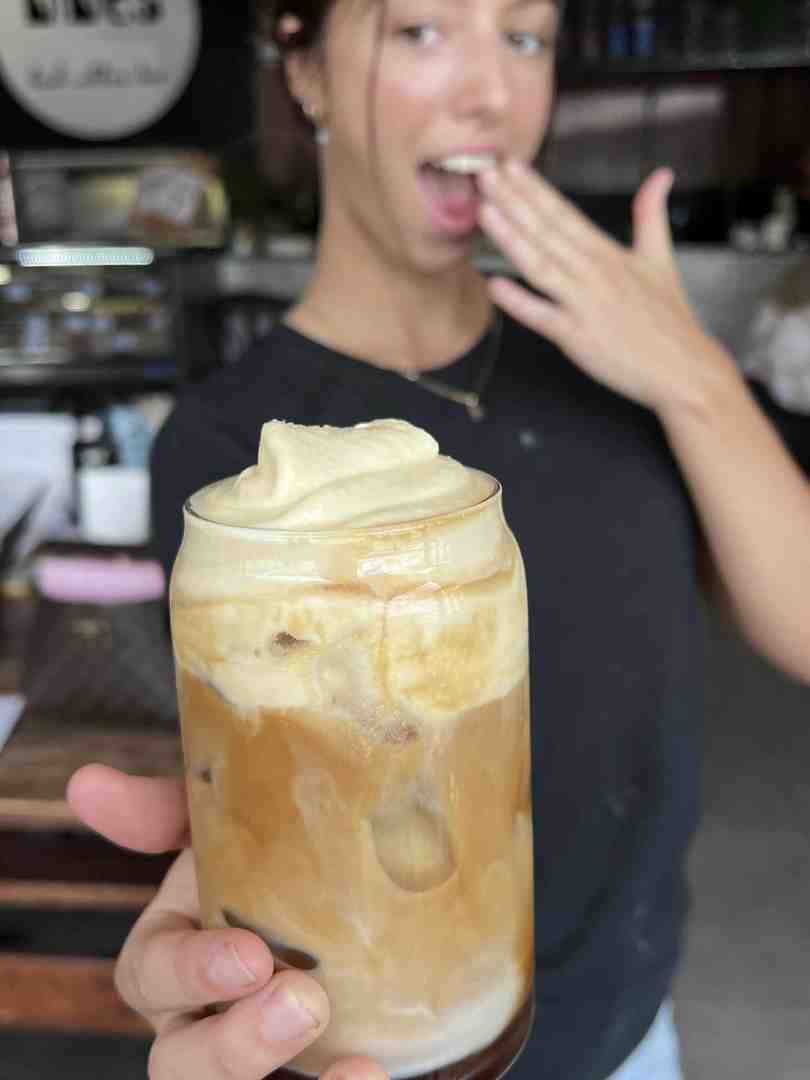 A barista excitedly presents a tall glass of specialty iced coffee topped with rich cold foam, illustrating the premium beverage offering and friendly service at The Nines, a work friendly cafe. A barista excitedly presents a tall glass of specialty iced coffee topped with rich cold foam, illustrating the premium beverage offering and friendly service at The Nines, a work friendly cafe.