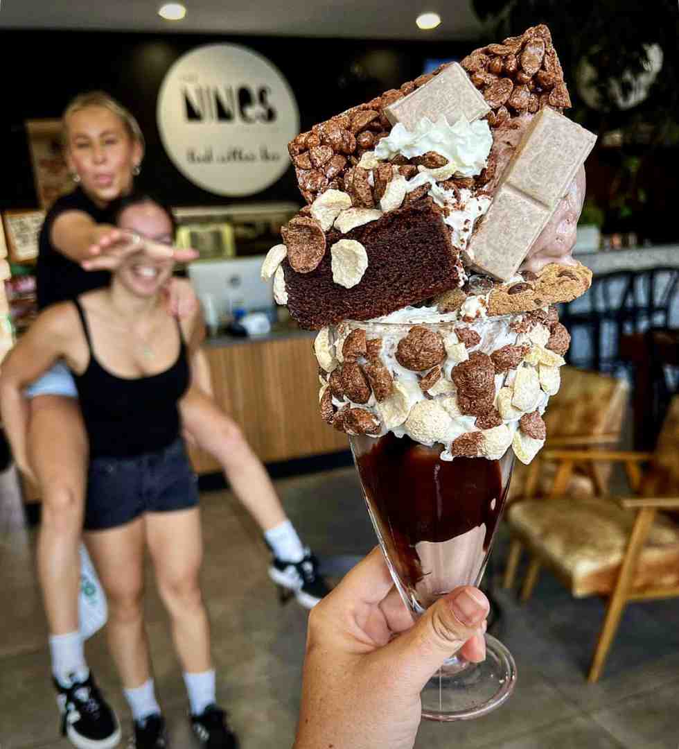 A massive, decadent chocolate milkshake loaded with brownie pieces, cereal, and cream, with two friends goofing off in the background. Find these unique treats at fun cafes in Maroochydore. A massive, decadent chocolate milkshake loaded with brownie pieces, cereal, and cream, with two friends goofing off in the background. Find these unique treats at fun cafes in Maroochydore.