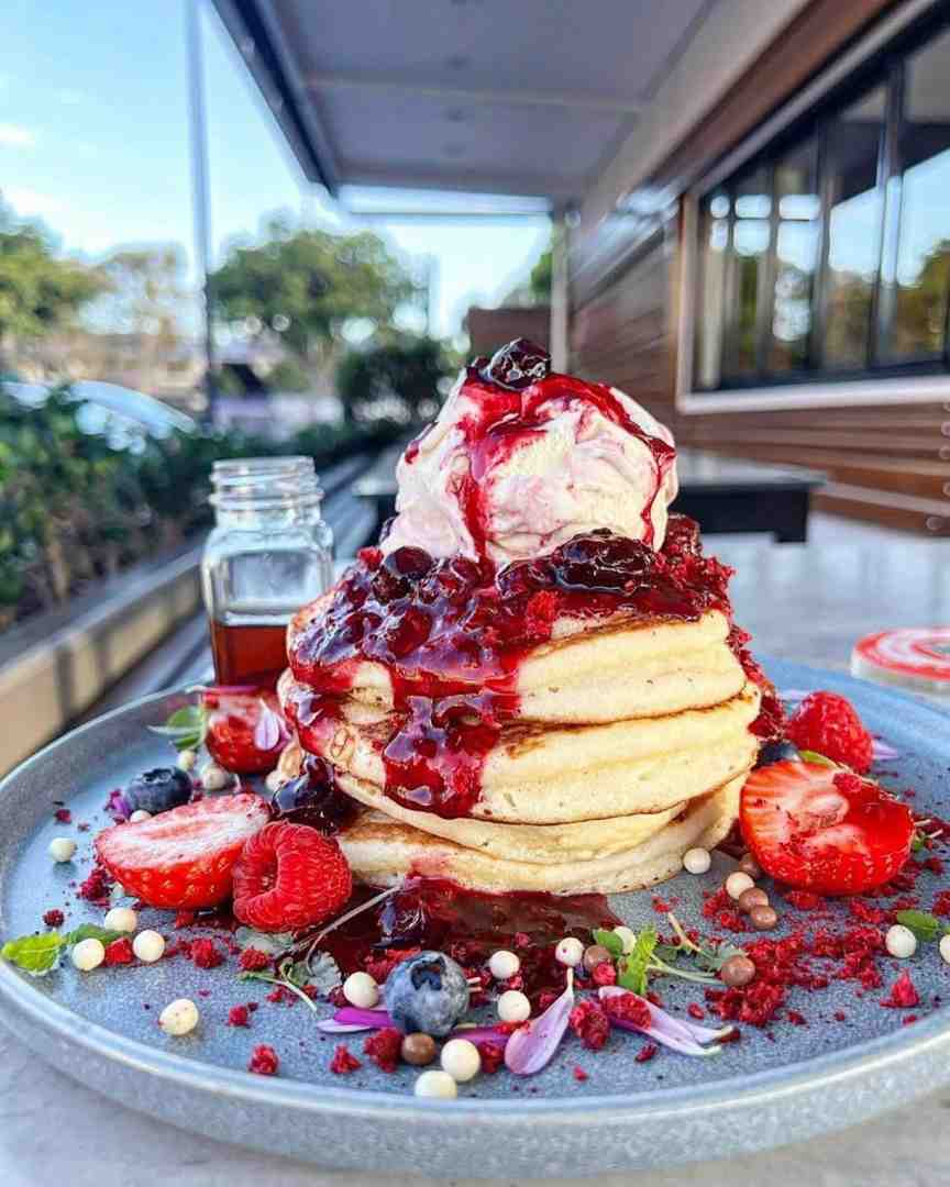 A towering stack of fluffy pancakes, smothered in rich berry compote, topped with ice cream, and garnished with fresh fruit, the ultimate choice when deciding on pancakes or waffles.