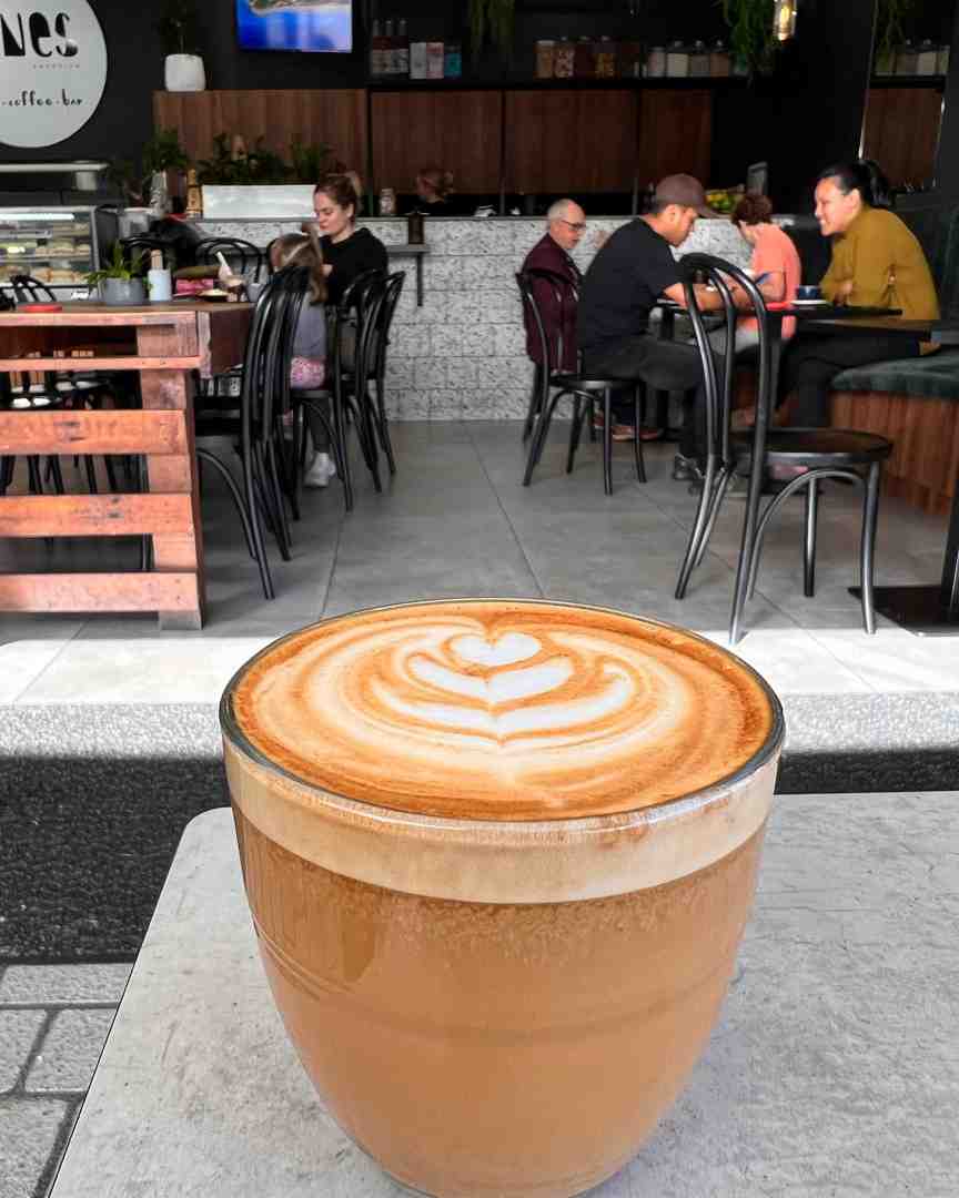 A large, clear glass mug of coffee displaying rich crema and expertly executed tulip latte art, enjoyed outside The Nines -Sunshine Coast best coffee